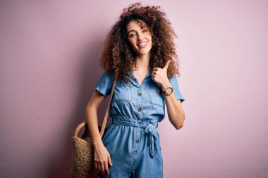 Kıvırcık saçlı, piercing takan, kot giyen ve hasır çantalı güzel bir kadın elinle mutlu bir jest yapıyor. Kameraya bakıp başarıyı gösteren ifade onaylanıyor.