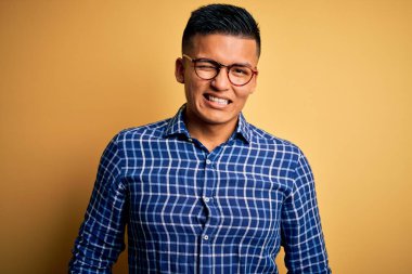 Genç, yakışıklı, latin gömlekli, sarı arka planda gözlüklü, seksi bir ifadeyle kameraya bakan, neşeli ve mutlu yüzlü bir adam..