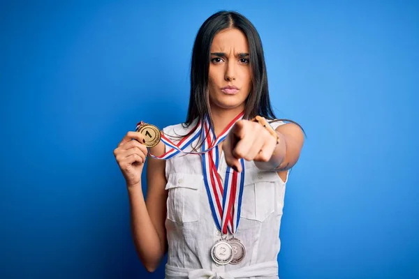 若い美しいブルネットは カメラとあなたに指を指している青い背景の上にメダルを受賞したチャンピオンの女性を打ち負かします 手のサイン 正とフロントからの自信を持ってジェスチャー — ストック写真