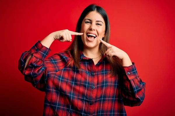 赤い背景にカジュアルなシャツを着た若い美しい女性が陽気で 指の歯と口を指差して笑っています 歯科衛生の概念 — ストック写真