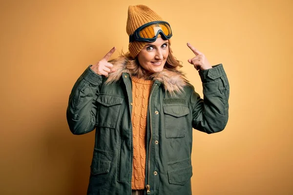 中年美丽的金发滑雪者女人穿着雪地运动鞋和滑雪护目镜 用双手指指着头 很好的主意或想法 很好的记忆力 — 图库照片