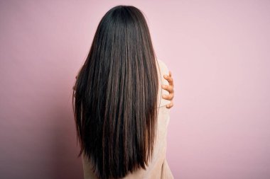 Genç, güzel Asyalı bir kadın pembe arka planda sıradan bir tişört giyip mutlu ve pozitif bir şekilde kendine sarılıyor. Sevgi ve özgüven.