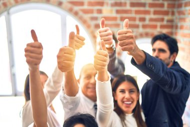 Bir grup iş adamı mutlu gülümsüyor. Ofiste baş parmaklarınla dikiliyorsun.