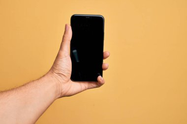 Kafkasyalı genç adam elinde akıllı telefonuyla izole edilmiş sarı arka planda ekranı gösteriyor.