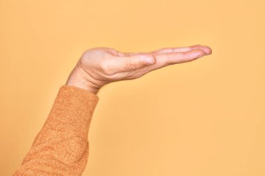 Beyaz bir gencin eli, izole edilmiş sarı arka plan üzerinde parmaklarını gösteriyor. Düz palmiye ürünü sunuyor, el hareketi yapıyor, boş kopya alanı veriyor.