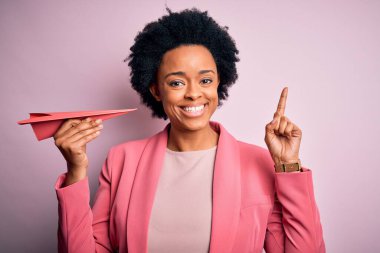 Pembe kâğıt uçak tutan kıvırcık saçlı, genç Afrikalı Afro kadın bir fikir ya da soru işareti ile şaşırdı.