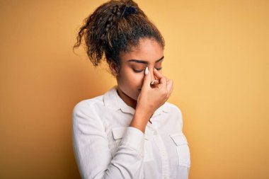 Genç, güzel, Afro-Amerikalı bir kız sarı arka plan üzerinde dikilmiş yorgun burnu ve gözleri ovuşturarak yorgunluk ve baş ağrısı hissediyor. Stres ve hüsran kavramı.
