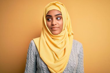 Genç, güzel, Afro-Amerikalı bir kız izole edilmiş sarı arka plan üzerine Müslüman başörtüsü takıyor. Gülümsüyor ve uzaklara bakıyor..