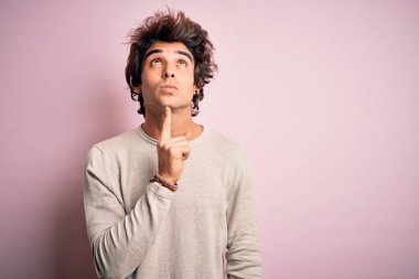 İzole edilmiş pembe arka plan üzerinde duran sıradan tişörtler giyen genç yakışıklı bir adam parmak çenesinde ve yukarı bakarak şüphe üzerine yoğunlaşmıştı.