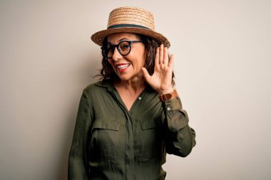 Orta yaşlı esmer kadın, gözlüklü ve şapkalı. İzole edilmiş beyaz arka planda dikiliyor. Kulaktan kulağa gülümsüyor. Sağırlık kavramı.