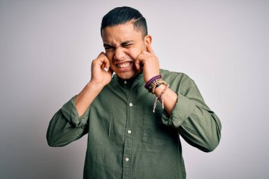 İzole edilmiş beyaz arka plan üzerinde dikilen Brezilyalı genç bir adam yüksek sesli müzik sesi için kulakları parmaklarıyla kapatıyor. Sağır kavramı.