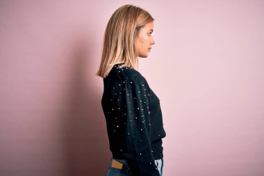 Pembe izole edilmiş arka planda moda süveteri giyen genç, güzel sarışın kadın yan yana bakıyor, rahat poz veriyor, kendine güvenen bir gülümsemesi var..