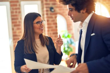 Two young beautiful business workers smiling happy and confident. Standing with smile on face working together speaking and reading documents at the office