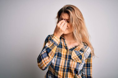 İzole edilmiş beyaz arka planda dikilen sıradan bir gömlek giyen genç ve güzel sarışın kadın yorgun burnu ve gözlerini ovuşturup yorgunluk ve baş ağrısı hissediyordu. Stres ve hüsran kavramı.