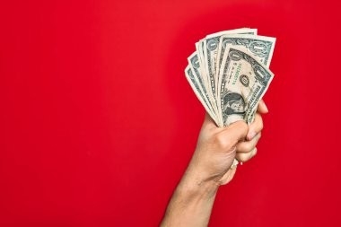 Güzel bir el, kırmızı arka planda bir deste dolar tutan bir adam.
