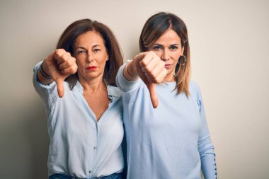 Orta yaşlı, güzel bir çift kız kardeş izole edilmiş beyaz arka planda duruyorlar mutsuz ve kızgın görünüyorlar, reddedilmişler ve olumsuz davranıyorlar. Kötü ifade.