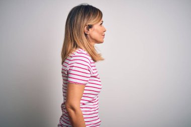 Orta yaşlı güzel bir kadın izole edilmiş beyaz arka plan üzerine sıradan çizgili tişört giyiyor, rahat bir görünüm takınıyor, kendine güvenen bir gülümsemeyle doğal bir yüz ifadesi sergiliyor..