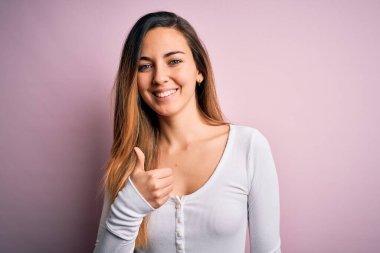 Pembe arka planda beyaz tişört giyen, mavi gözlü genç, güzel sarışın bir kadın elinle mutlu bir jest yapıyor. Kameraya bakıp başarıyı gösteren ifade onaylanıyor.