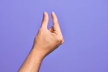 İzole edilmiş mor arka plan üzerinde parmaklarını gösteren beyaz bir adamın eli. Görünmez bir şeyi alıyor, parmakları boşluğu gösteren bir nesneyi tutuyor.