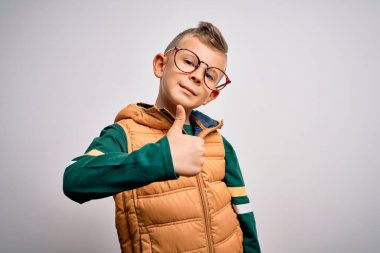 Mavi gözlü, kışlık paltolu ve gözlüklü, mutlu bir el hareketi yapan küçük beyaz bir çocuk. Kameraya bakıp başarıyı gösteren ifade onaylanıyor.