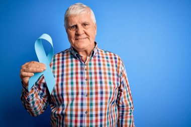 Üst düzey yakışıklı, elinde mavi kanser kurdelesi olan, mutlu bir yüzü olan, kendine güvenen, gülümseyen, dişlerini gösteren bir adam.