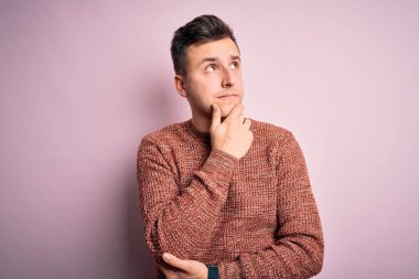 Pembe soyutlanmış arka plan üzerine sıradan bir kazak giyen yakışıklı beyaz bir adam bir soru hakkında endişeli ve gergin bir şekilde düşünüyor.