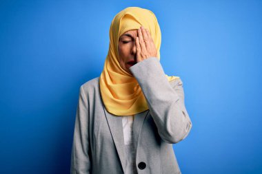 Orta yaşlı esmer bir iş kadını mavi arka plan üzerine geleneksel başörtüsü takıyor. Yarı yüz, göz ve ağzı elle kapatmaktan yorulmuş. Yüzüm acıyor..