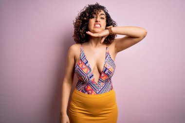 Genç, güzel bir Arap kadın, mayo ve pembe arka planda güneş gözlüğü takmış, boğazını bıçak gibi kesiyor, saldırganlığı şiddetli bir şiddetle tehdit ediyor.