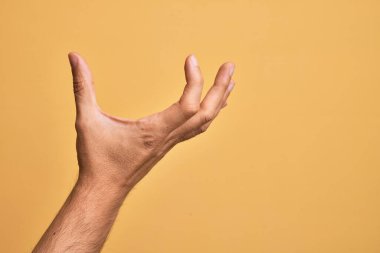 İzole edilmiş sarı arka plan üzerinde parmaklarını gösteren beyaz bir adamın eli. Görünmez bir şeyi alıp, parmaklarıyla uzayı gösteren bir nesneyi tutuyor.