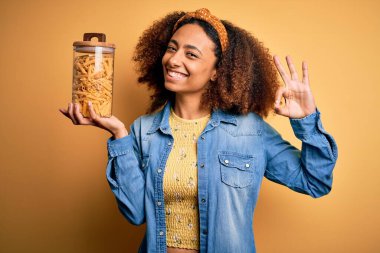 Afro saçlı, sağlıklı makarna dolu kavanozu olan Afro Amerikalı genç bir kadın parmaklarıyla imza atıyor. Mükemmel bir sembol.