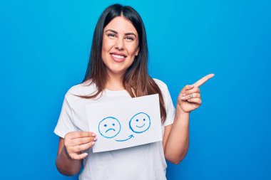 Kadın psikoloji değişikliği istiyor. Elinde mutsuz ve mutlu bir duygu mesajı olan bir kağıt tutuyor. Gülümsüyor, elini ve parmağını yana uzatıyordu.