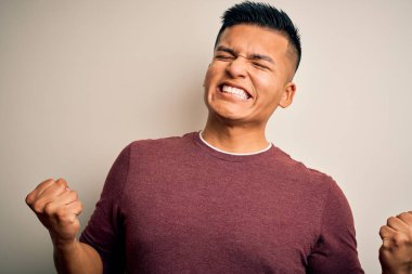 İzole edilmiş beyaz arka planda dikilen gündelik süveter giyen genç, yakışıklı Latin adam mutlu ve heyecanlı bir şekilde kollarını kaldırıp, gülümseyip başarı için bağırıyor. Kutlama konsepti.