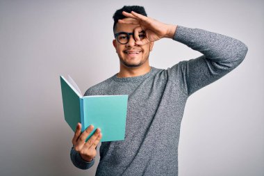 Genç, yakışıklı, zeki bir öğrenci, izole edilmiş beyaz arka planda kitap okuyor. Mutlu bir yüzü var. Gülümsüyor.
