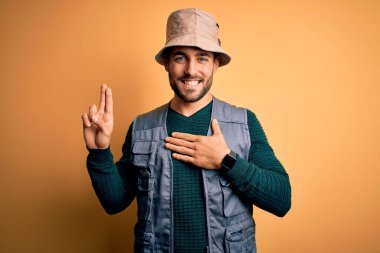 Tatilde sakallı yakışıklı bir turist sarı arka planda kaşif şapkası takıyor. Gülümsüyor, yemin ediyor.