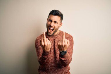 Young handsome man wearing casual sweater standing over isolated white background Showing middle finger doing fuck you bad expression, provocation and rude attitude. Screaming excited