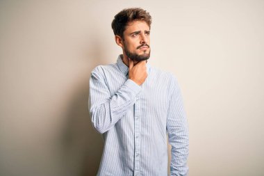 Beyaz arka planda duran çizgili tişörtlü, sakallı, yakışıklı genç bir adam boynu ağrıyan, boğazı ağrıyan, grip, mantar ve enfeksiyon kapmış.