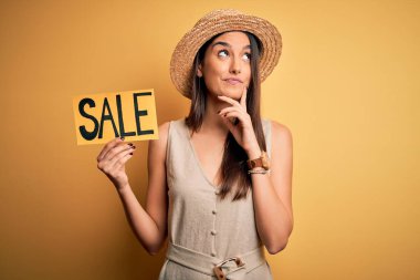 Sarı arka planda şapka taşıyan esmer, güzel bir kadın. Ciddi bir yüz ifadesi var. Soru sormayı düşünüyor.