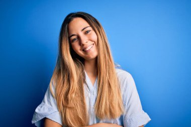 Mavi arkaplanda çizgili tişört giyen, kollarını kavuşturup kameraya gülümseyen güzel sarışın kadın. Pozitif kişi.