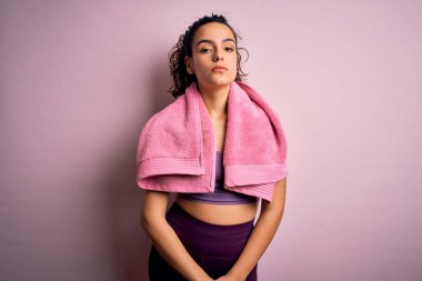 Kıvırcık saçlı, spor yapan, pembe arka planda havlu kullanan genç ve güzel bir sporcu. Yüzünde ciddi bir ifadeyle rahatlamış. Basit ve doğal bir şekilde kameraya bakıyorsun..