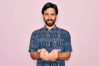 Pembe arka planda hippi tarzı giyinmiş, elleri avuçlarında gülümseyen ya da el hareketi yapan yakışıklı İspanyol bohem bir adam. Tutun ve koruyun
