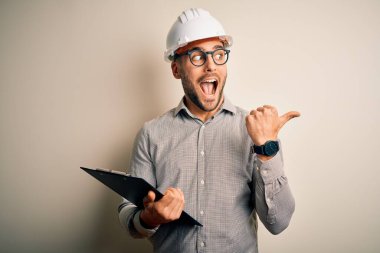 Mimar müfettiş, miğfer takıyor ve pano kullanıyor. Başparmağıyla işaret ediyor ve gülümsüyor.