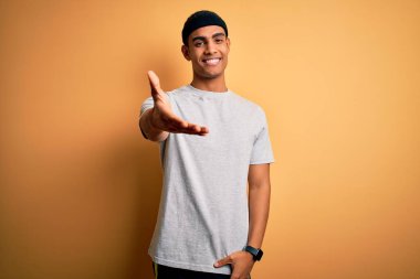 Yakışıklı Afro-Amerikan sporcusu sarı arka planda spor giysisi giyiyor neşeli gülümseyerek avuç içi yardım ve kabullenme sunuyor..