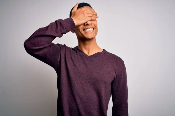 白い背景にカジュアルなセーターを着た若いハンサムなアフリカ系アメリカ人男性が笑顔で 驚きのために目を覆う顔を手で笑っています ブラインドコンセプト — ストック写真