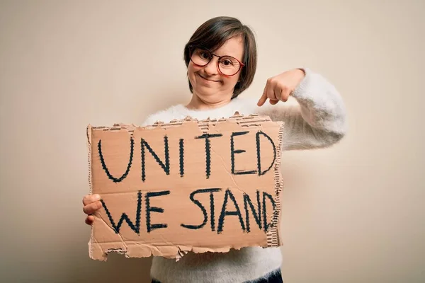 Young down syndrome woman holding protest banner with united we stand rights message with surprise face pointing finger to himself