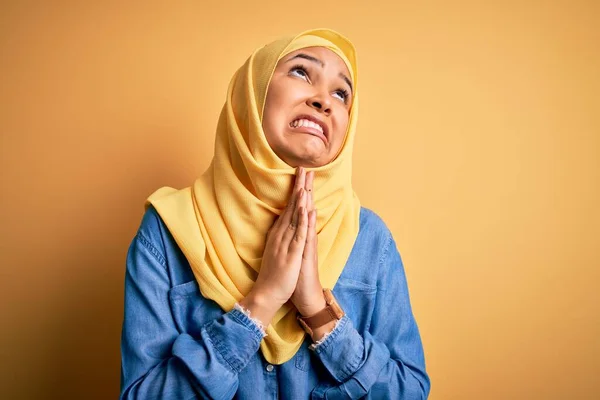 黄色の背景物乞いや手で祈る上でアラブの伝統的なヒジャーブを身に着けている巻き毛を身に着けている若い美しい女性と一緒に顔に希望の表現は非常に感情的かつ心配 物乞い — ストック写真