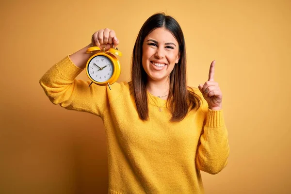 Jonge Mooie Vrouw Met Wekker Staande Geïsoleerde Gele Achtergrond Verrast — Stockfoto