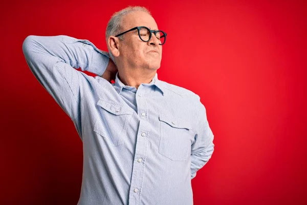 Middle age handsome hoary man wearing casual striped shirt and glasses over red background Suffering of neck ache injury, touching neck with hand, muscular pain