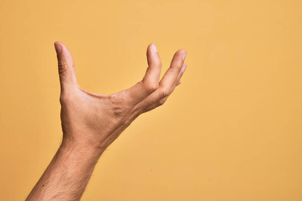 Hand of caucasian young man showing fingers over isolated yellow background picking and taking invisible thing, holding object with fingers showing space