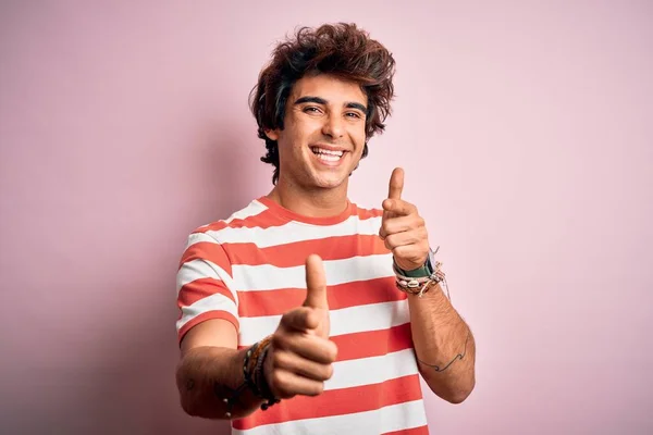 縞模様のカジュアルなTシャツを着た若いハンサムな男は 幸せと面白い顔を持つカメラに指を指して孤立したピンクの背景の上に立っている 良いエネルギーと振動 — ストック写真