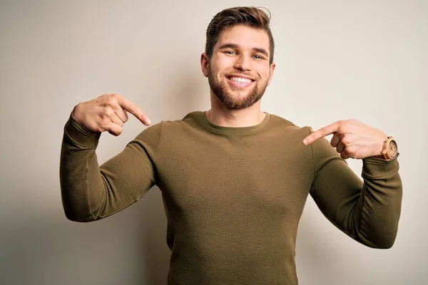 Young blond man with beard and blue eyes wearing green sweater over white background looking confident with smile on face, pointing oneself with fingers proud and happy.